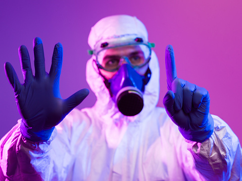 Coronavirus covid-19 pandemic. Doctor scientist wearing protective biological suit and mask due to global healthcare epidemic warning and danger background in blue and pink neon lights background