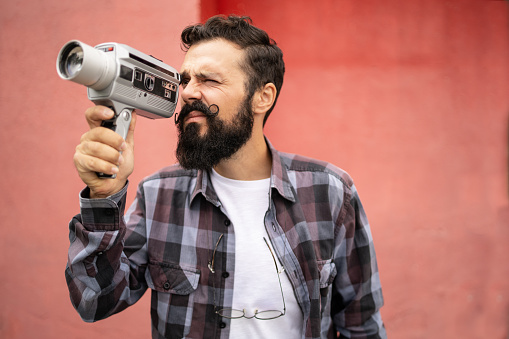 A young hipster man shooting video with a retro camera