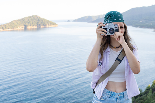 Young girl with a bandana is making photos with a vintage camera of the sea in Greece