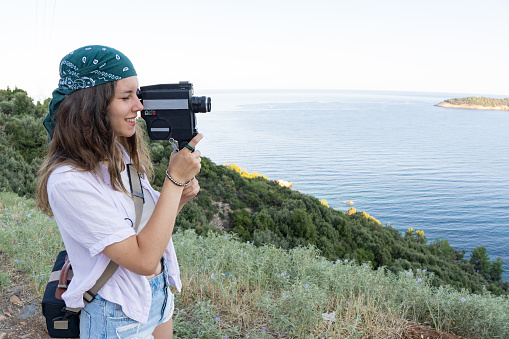 A teen girl is filming with a retro camera on her vacation
