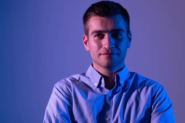 A man in a shirt poses on a dark multicolored neon background