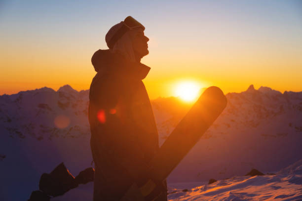 silhouette of a skier with skis standing on a slope at sunset against a mountain range. sportsman portrait stock photo