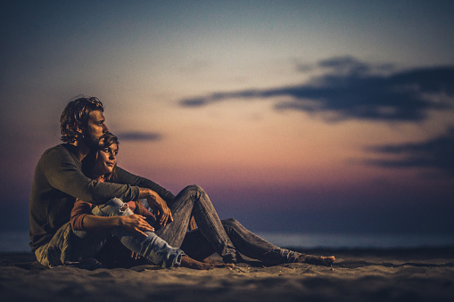 Young loving couple relaxing on the beach at dusk. Copy space.