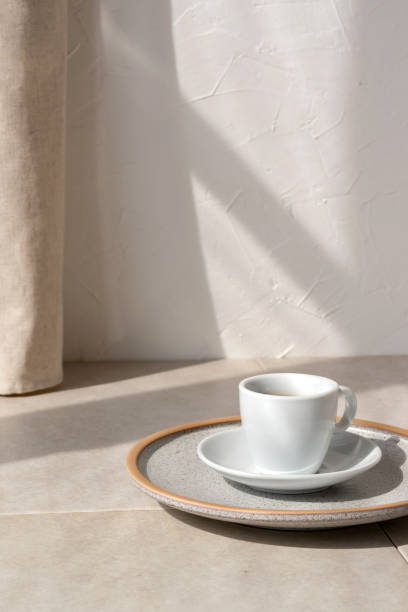 istock Coffee cup on a plate, on beige table, empty white wall background with lifestyle sunlight shadow, good morning concept, copy space 1489057790