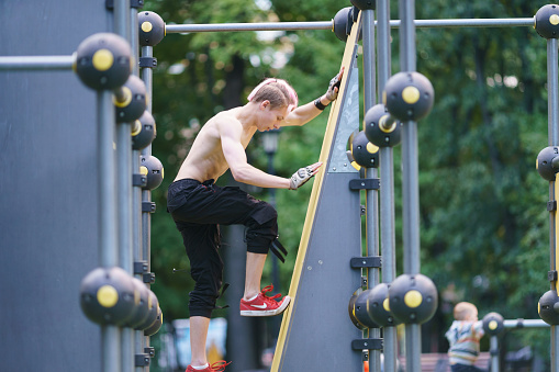 Moscow, Russia - August 9, 2022: Young great sport man does parkour on the city sport ground. He climbs a vertical wall. Extreme sports are very popular among youth. Low angle view