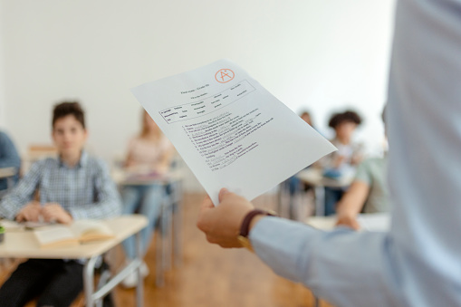 Cropped image of teacher standing in front of students with test results in her hand. Education, elementary school, teaching and people concept