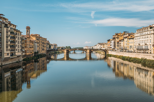 Gorgeous view of an old stone bridge across a river in Italy on a sunny warm summer evening on a blue sky. The concept of historical important infrastructural structures in Europe. Copyspace.
