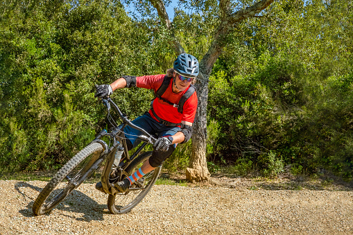 Mountain biker takes a turn at an angle and in a professional position. Very sporty and dynamic image that reproduces downhill or enduro and downhill mountain biking well. Tuscany, Italy, Europe