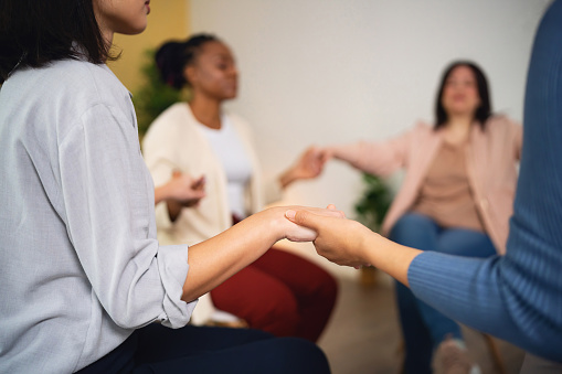 While sitting in a circle, multiracial group of women and men, having group therapy, while holding hands