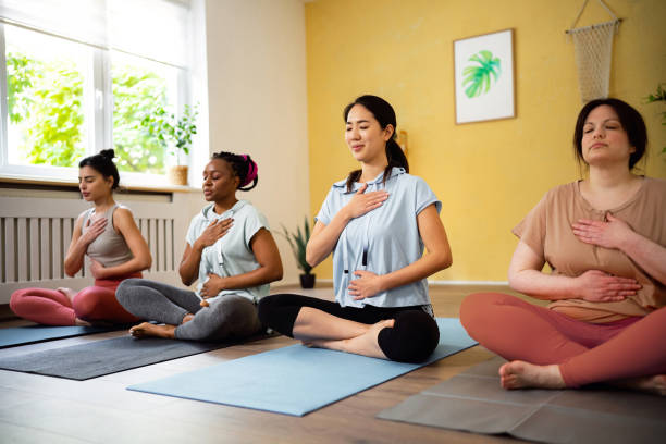 Multiracial women, meditating in lotus position, during group yoga class