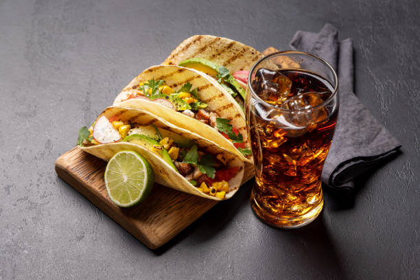 Mexican food featuring tacos with meat and grilled vegetables and glass of cola with ice