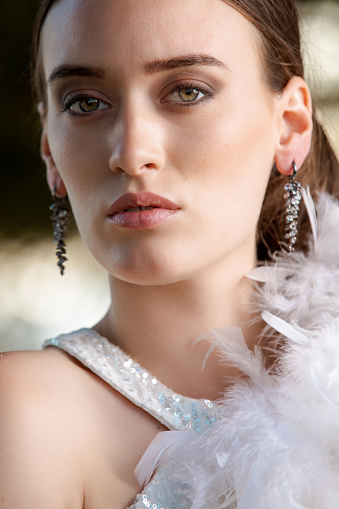 Headshot of beautiful young woman with feather boa on shoulder, standing outdoors and looking at camera, beauty and fashion industry