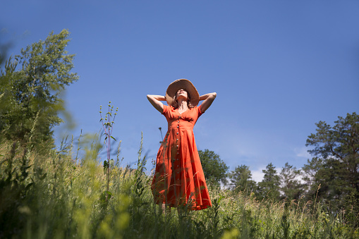 Slow life. Enjoying the little things. spends time in nature in summer. happy middle aged woman wearing an orange dress and straw hat relaxed outdoors. copy space. concept without stress. mental healt