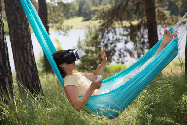 istock middle aged woman playing game in virtual reality glasses in a hammock relaxed outdoors. copy space. 1489075169