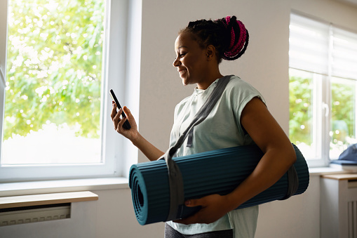 Side-view of woman Black ethnicity, using mobile phone at the yoga studio