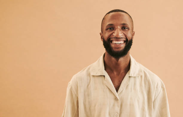 istock Black man smiling directly into the camera whilst standing in front of a brown background with a beard and a mustache with copy space stock photo 1489077955