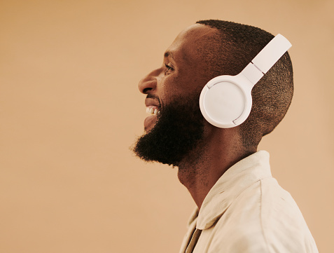 Profile shot of a happy young black man listening to music whilst smiling and laughing and wearing headphone, with copy space, stock photo