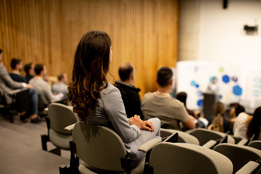 Pretty young woman sitting in audience on conference or workshop