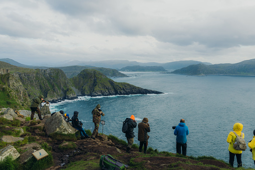 June 18, 2022: Group of tourists birdwatching with cameras with background view of ocean and islands on Runde island, Møre og Romsdal, Western Norway