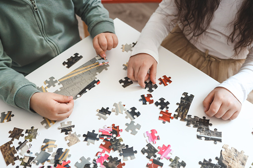 Brother and sister playing puzzles at home. Children connecting jigsaw puzzle pieces in a living room table. Kids assembling a jigsaw puzzle. Fun family leisure.