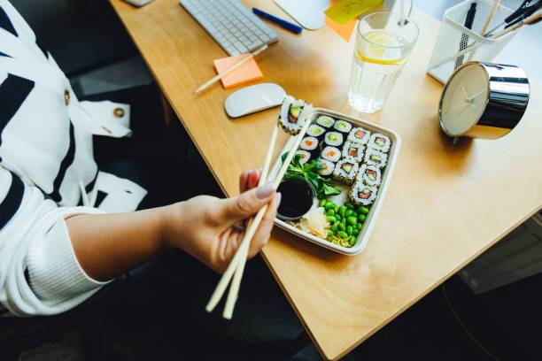 a person eating sushi at a computer table with some chopsticks