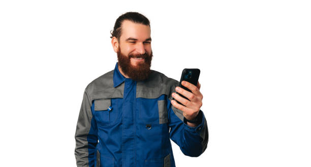 Handsome smiling young handyman in uniform has got a new client over the phone. stock photo