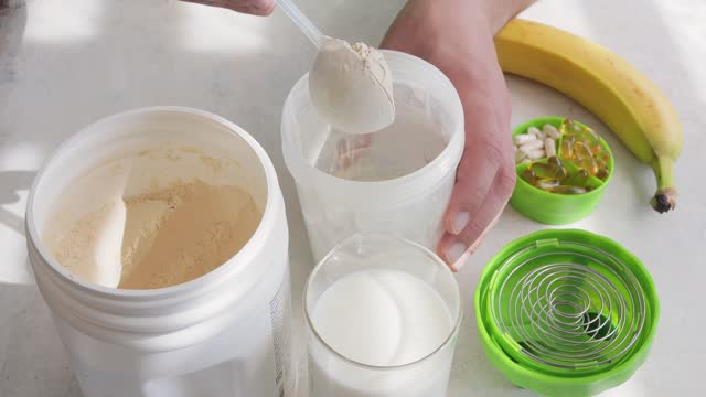 Male hand puts scoop with white whey or soy protein powder from a jar into plastic shaker, process of making protein smoothie drink, sport nutrition