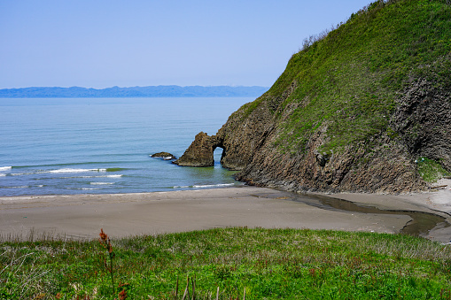 On a sunny day in April 2023, along Route 402 in Niigata City, Niigata Prefecture,\nEchigo Nanaura Seaside Line Kakumihama sea cave with Sado Island in the background