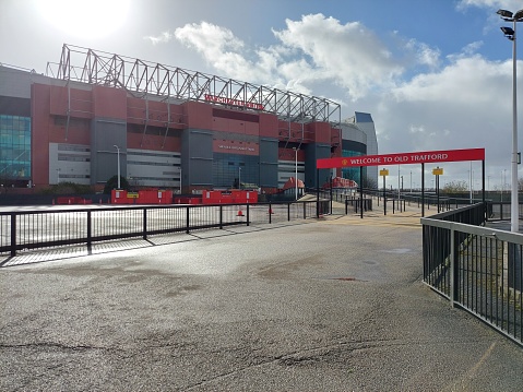 Image show one gate of Sir Alex Ferguson Stand  on Old Trafford Football Stadium of Manchester United FC. Sir Alex Ferguson is one of legend MU manager who brought MU get many trophies in 1986 - 2013 tenure. Weather during image created in the morning is sunny after rain. Image was created on 25 February 2022