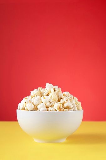Fresh popcorn in a bowl on red background and yellow table with copy space