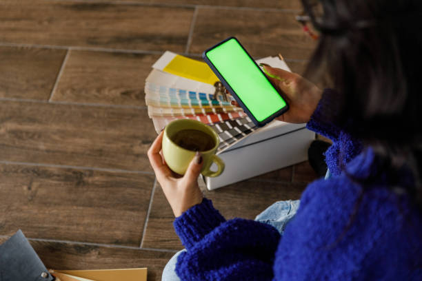 istock Young woman having coffee and using smart phone with chroma key on the screen when moving into new home 1489094565