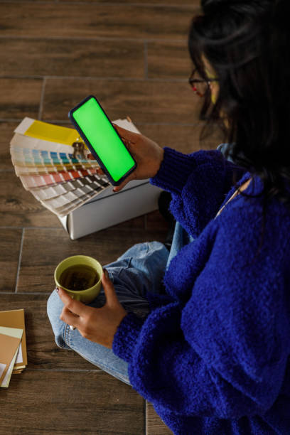 istock Young woman having coffee and using smart phone with chroma key on the screen when moving into new home 1489094625