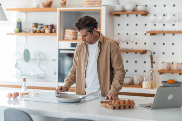 istock A hungry male freelancer makes scrambled eggs for breakfast while working on a laptop. 1489095481
