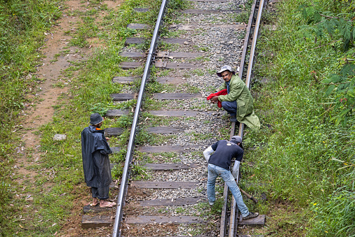 Demodara railway loop, Uva Province, Sri Lanka - February 19th 2023:  Two men working on the railroad track while a college is keeping outlook for eventually approaching trains