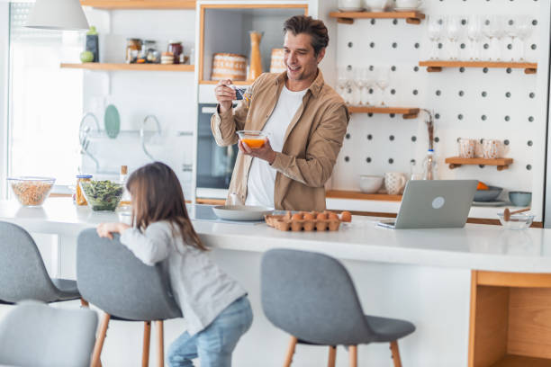 istock A smiling father freelancer making eggs for breakfast for his daughter and working on a laptop. 1489095683