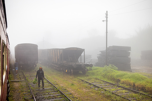 Ambewela Station, Uva Province, Sri Lanka - February 19th 2023:  Man trying to sell fresh vegetables to the passengers in a standing train on a rainy and foggy day