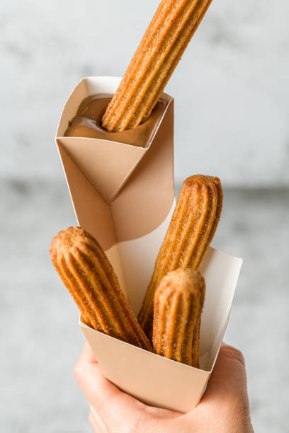 istock Woman taking churros from a cone and dipping it in chocolate sauce 1489097463