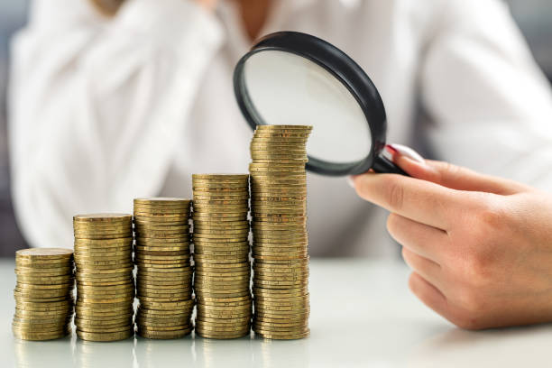 istock female boss looking through a magnifying glass at a stack of coins on the table. 1489097671