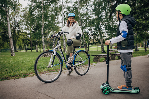 Mother and her son driving bikes and push scooter in the park with safety equipment