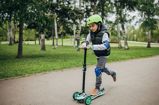 Little boy riding a push scooter in the park