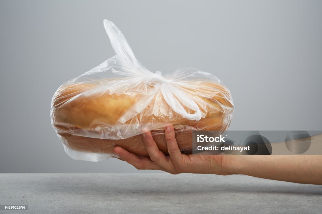Hand holding a whole bread in plastic bag over the table Bag Stock Photo
