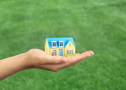 Small home model on the hand of women on green grass background .  Human holding the property on hand with finance concept.