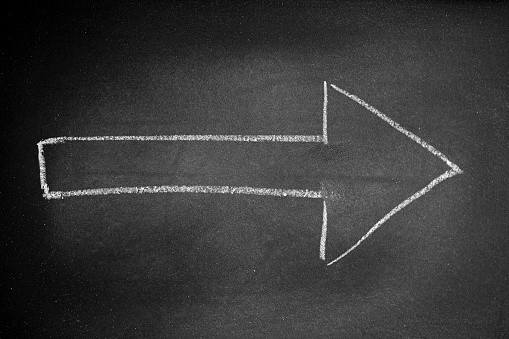 White arrow drawn on a black board with chalk indicating a direction