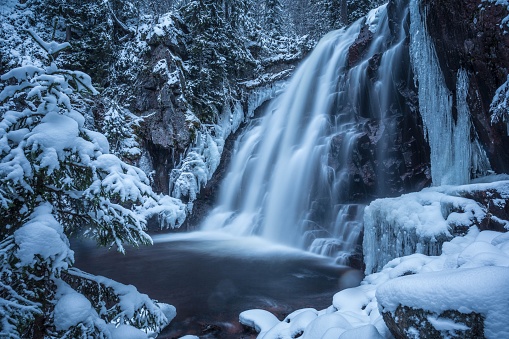A picturesque winter scene featuring a frozen waterfall cascading through a snowy forest