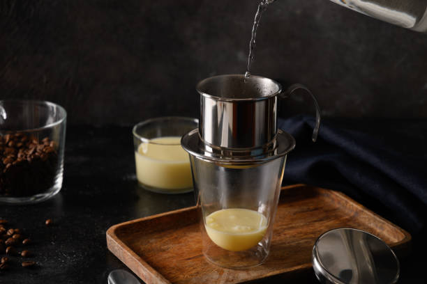 Pouring water in drip filter for cooking Vietnamese coffee with sweet condensed milk.