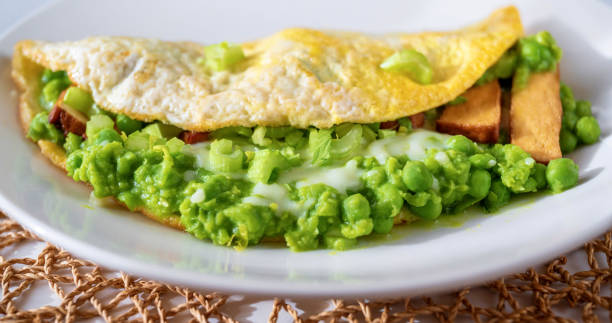 istock Egg omelette, mashed fresh green pea, celery stalk, smoked tofu on white plate on bamboo pad, closeup. 1489106465