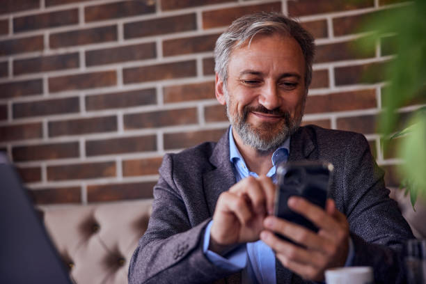 istock Smiling senior businessman using his mobile phone while sitting and working at his restaurant. 1489111578