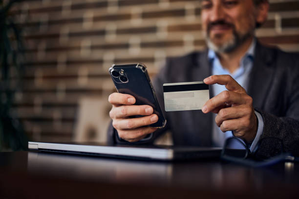 istock A smiling businessman is online shopping on a mobile phone, using a card. 1489111648