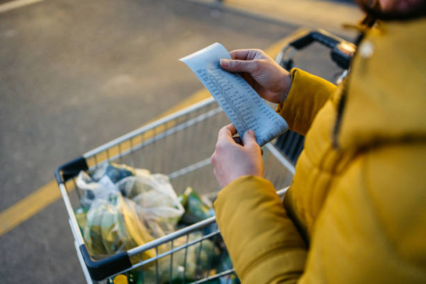 young woman looking at the receipt from the grocery store - shopping basket imagens e fotografias de stock