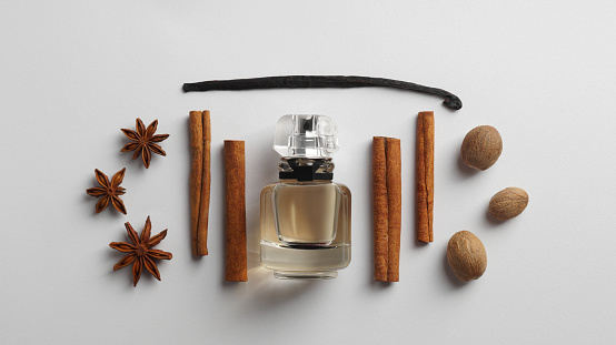Bottle of perfume surrounded by different spices on white background, top view